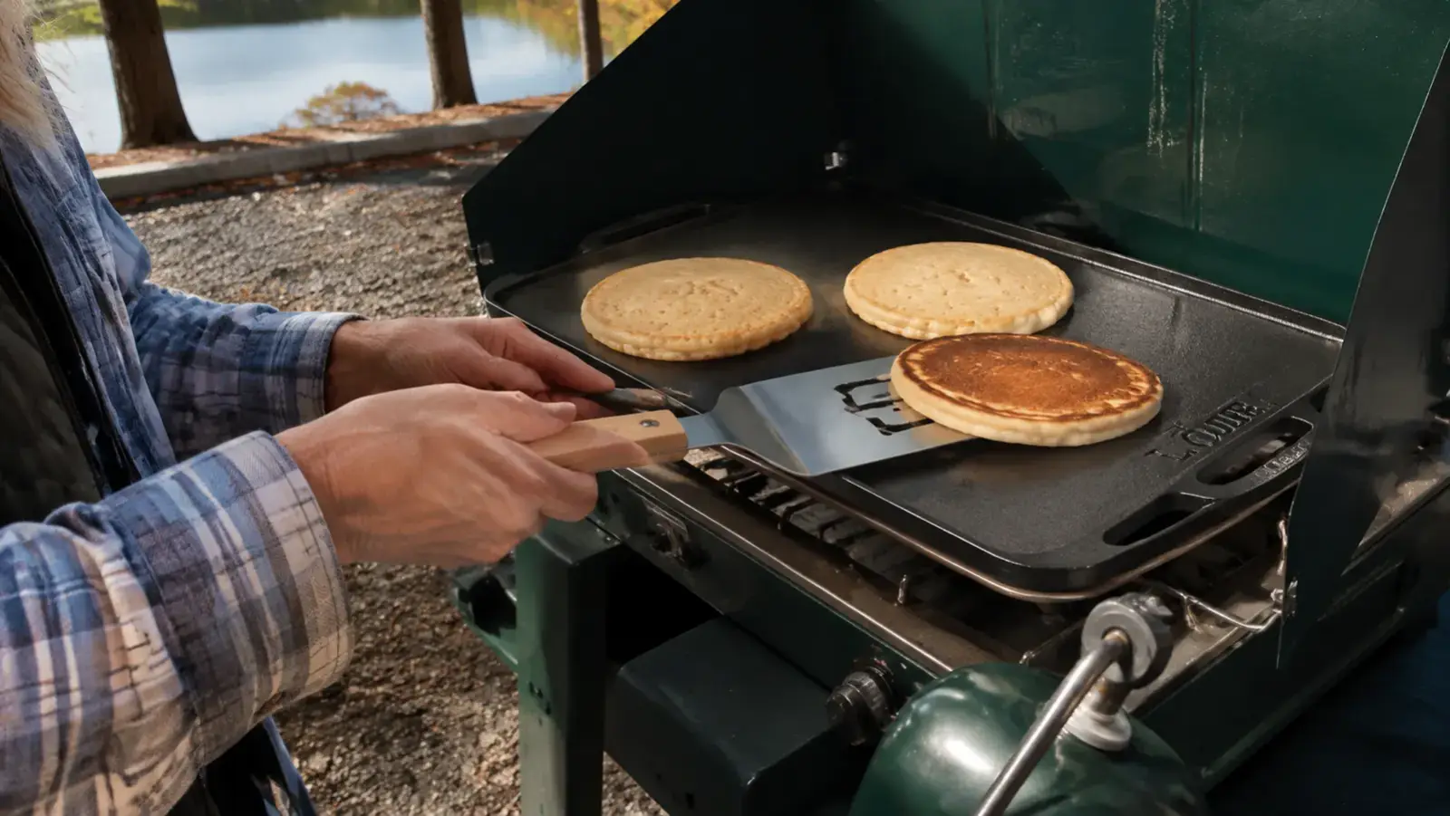Close-up of hands sliding a spatula under pancakes on a reversible cast iron griddle pan